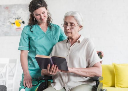 senior-woman-sitting-wheelchair-reading-book-with-nurse-standing_23-2147861517.jpg